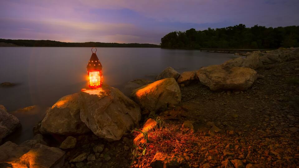 Blue Springs Lake located outside of Kansas City, Missouri at night with a lantern glowing light onto the rocky shoreline; Shutterstock ID 282722099