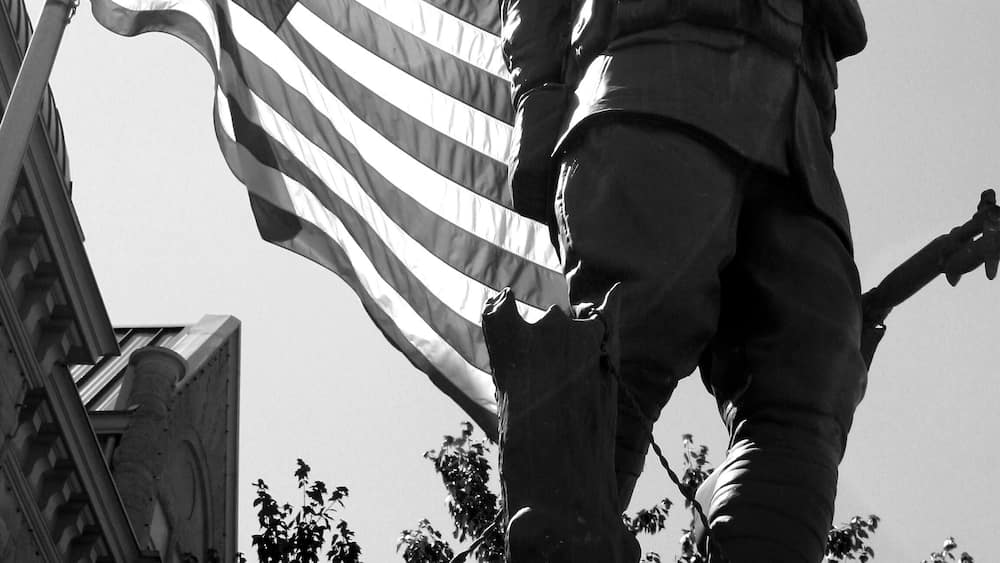 A statue of a soldier with raised fist, an American flag, and a building in the background.