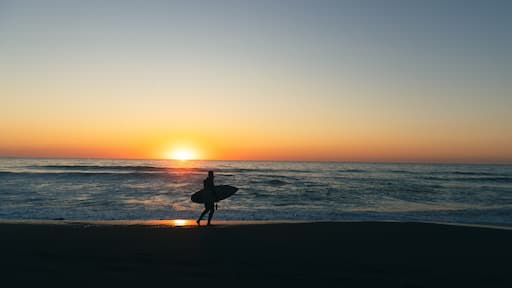 Surfer holding surfboard on a beach with the sunset in the background.