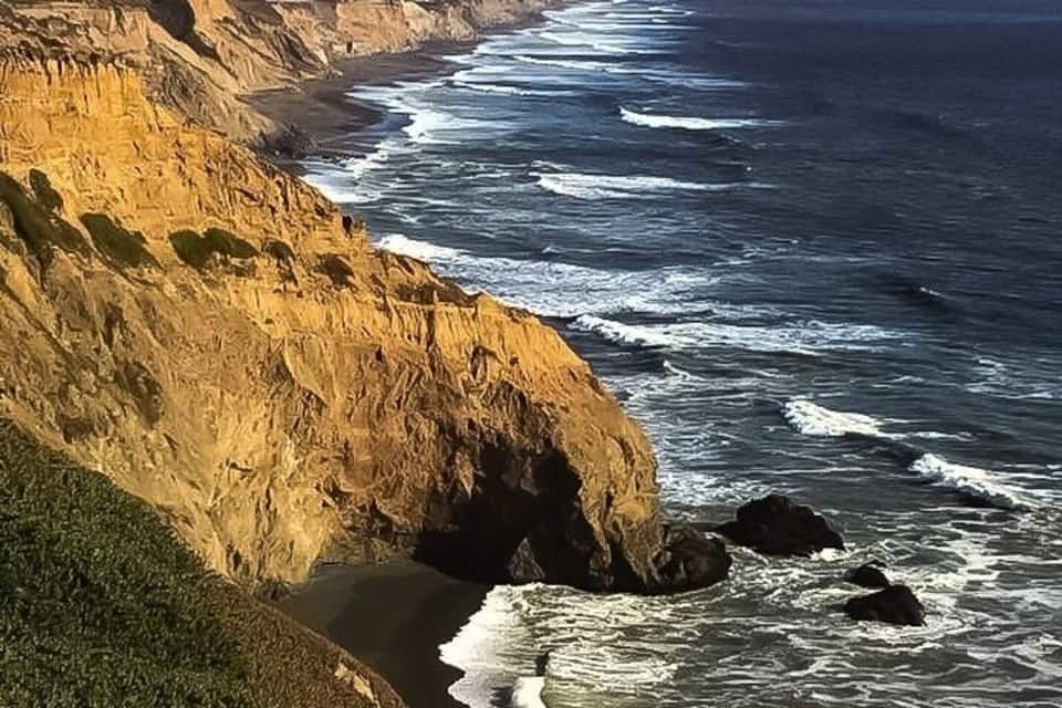 A coastal landscape with cliffs, ocean waves, and distant mountains.