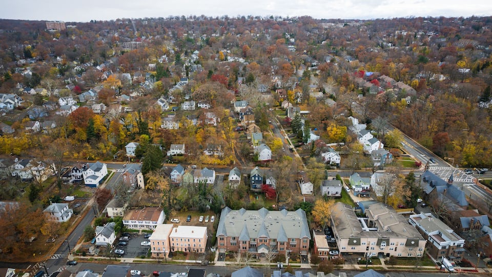 An aerial view of a residential area with houses, roads, and autumn-colored trees.