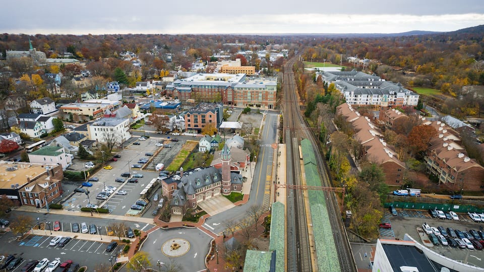 An aerial view of a town with a train track, parking lots, and various buildings.