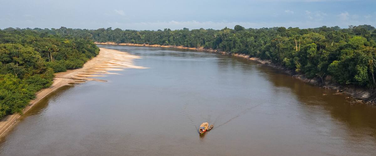 A river with a boat in the middle, surrounded by dense green forest.