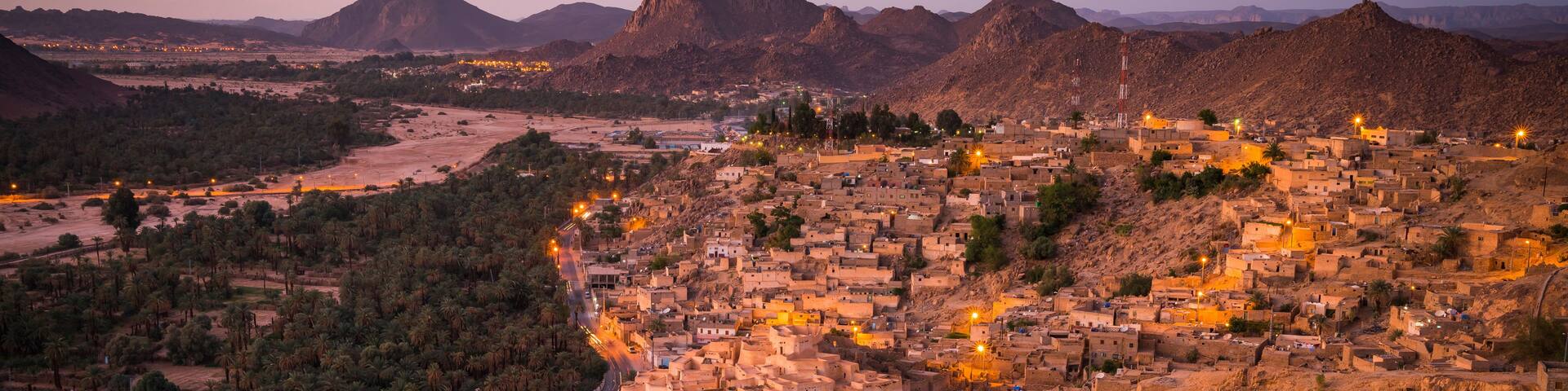 A mountainous landscape with a town at dusk, featuring illuminated buildings and a clear sky.