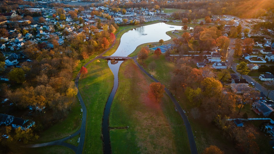 An aerial view of a town with a river, a bridge, and autumn-colored trees.