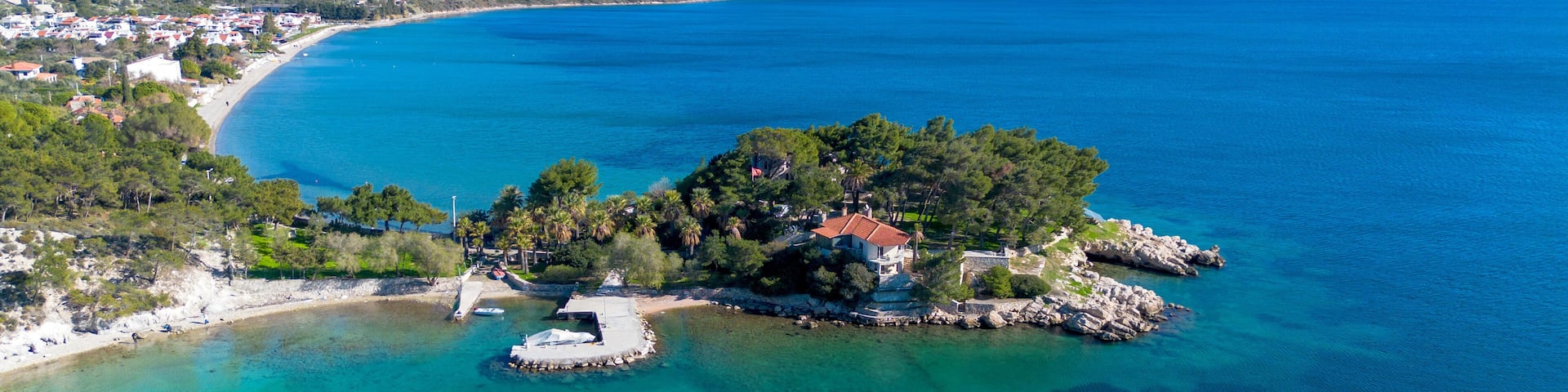 An aerial view of a coastal town with a prominent island featuring a red-roofed building surrounded by lush greenery.