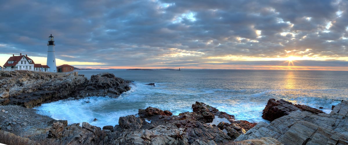 A lighthouse, rocky coastline, and a sunset over the ocean.
