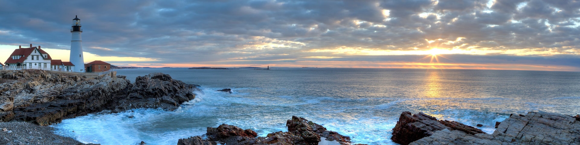 A lighthouse, rocky coastline, and a sunset over the ocean.