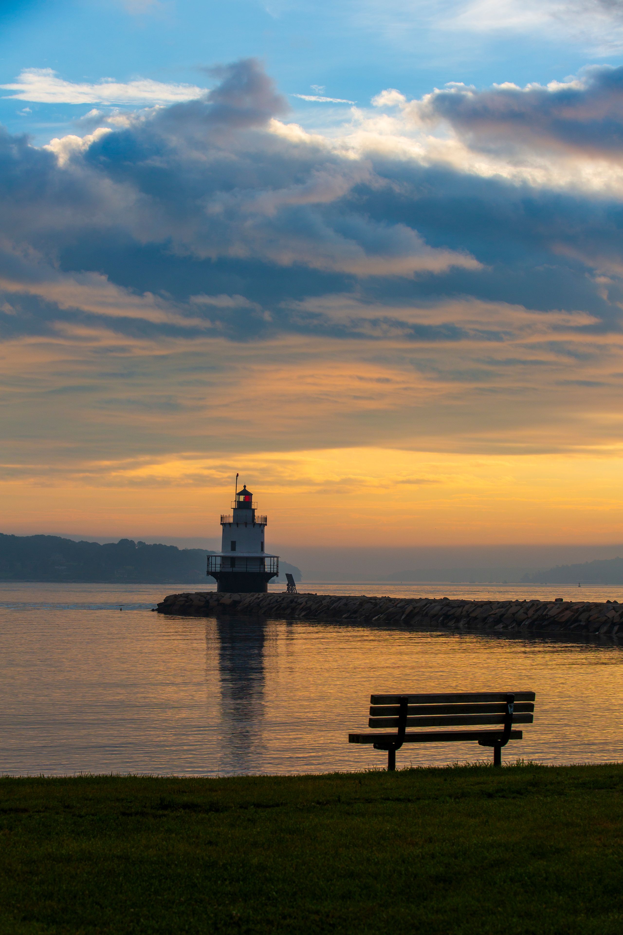 A lighthouse on a rocky outcrop with a bench in the foreground.