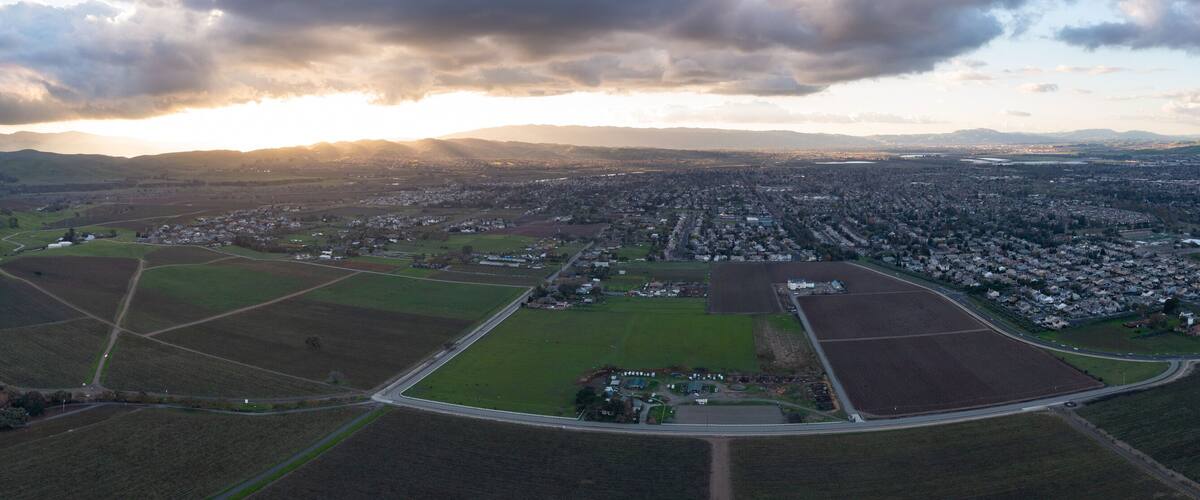 An aerial view of a rural landscape with rolling hills, fields, and a small town with houses and roads.