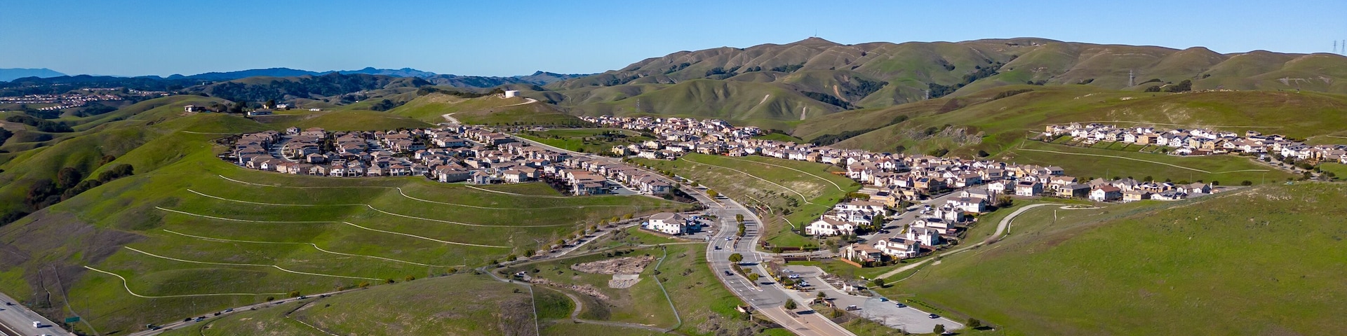 Aerial images over the green hills in Dublin, California with Real Estate in the background and a blue sky