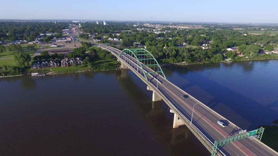 A green bridge over a river with a town in the background.