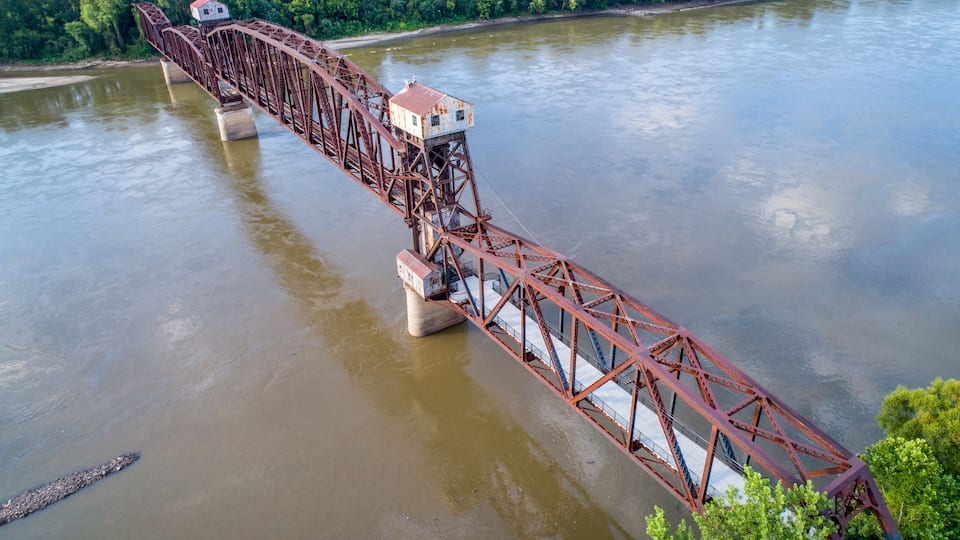 A large red metal bridge spanning a river with a small house on top.