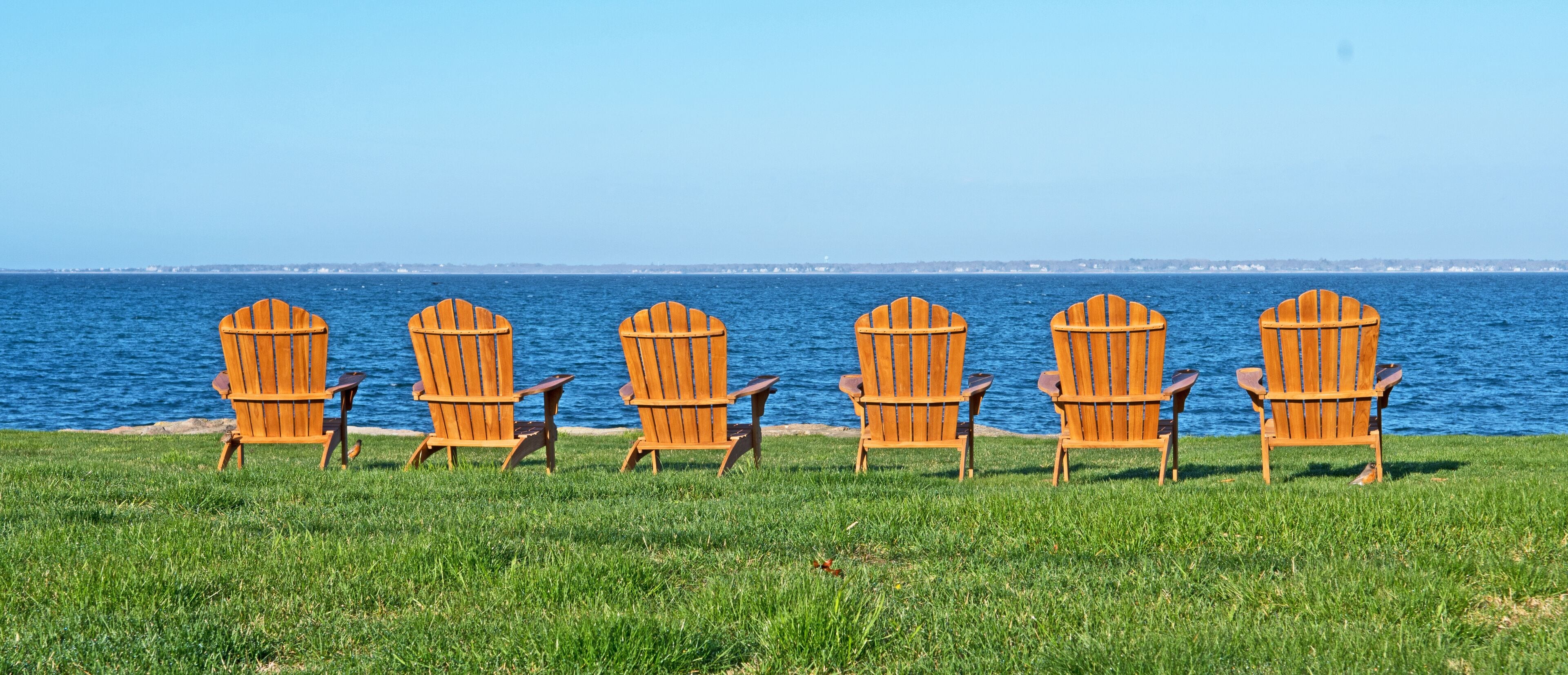 Six adirondack style chairs are set on a lawn and facing Buzzard's Bay in Fairhaven, Massachusetts.