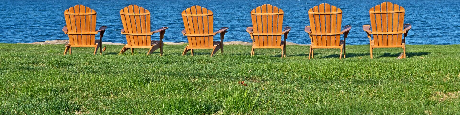 Six adirondack style chairs are set on a lawn and facing Buzzard's Bay in Fairhaven, Massachusetts.