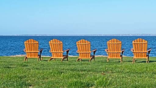 Six adirondack style chairs are set on a lawn and facing Buzzard's Bay in Fairhaven, Massachusetts.