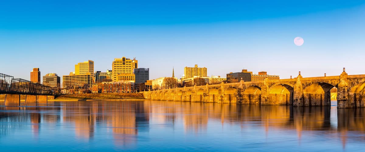 A city skyline with a historic stone bridge over a calm river, reflecting the buildings and the moon in the sky.