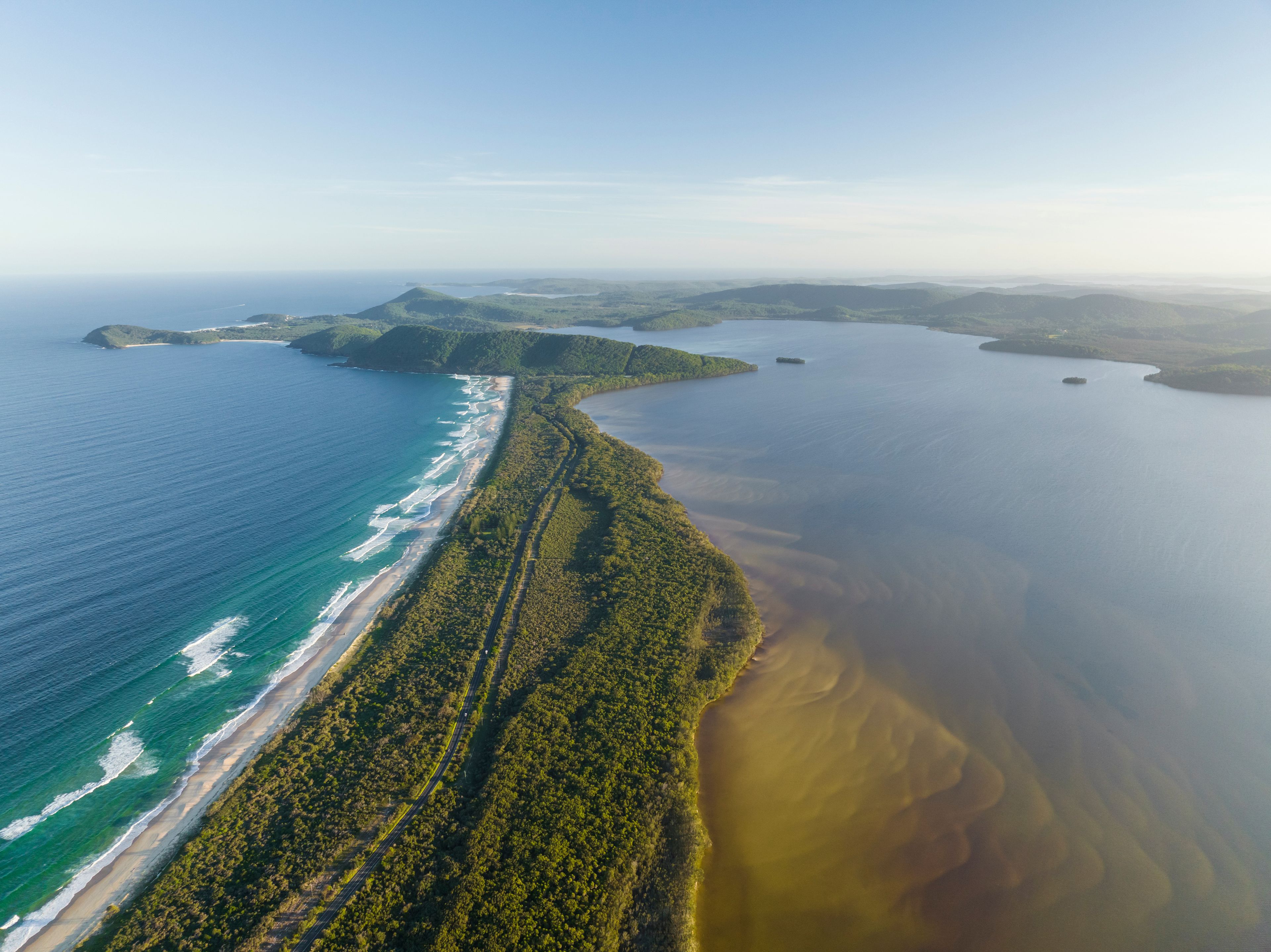 An aerial view of a coastal landscape with a beach, dense forest, and a large body of water.