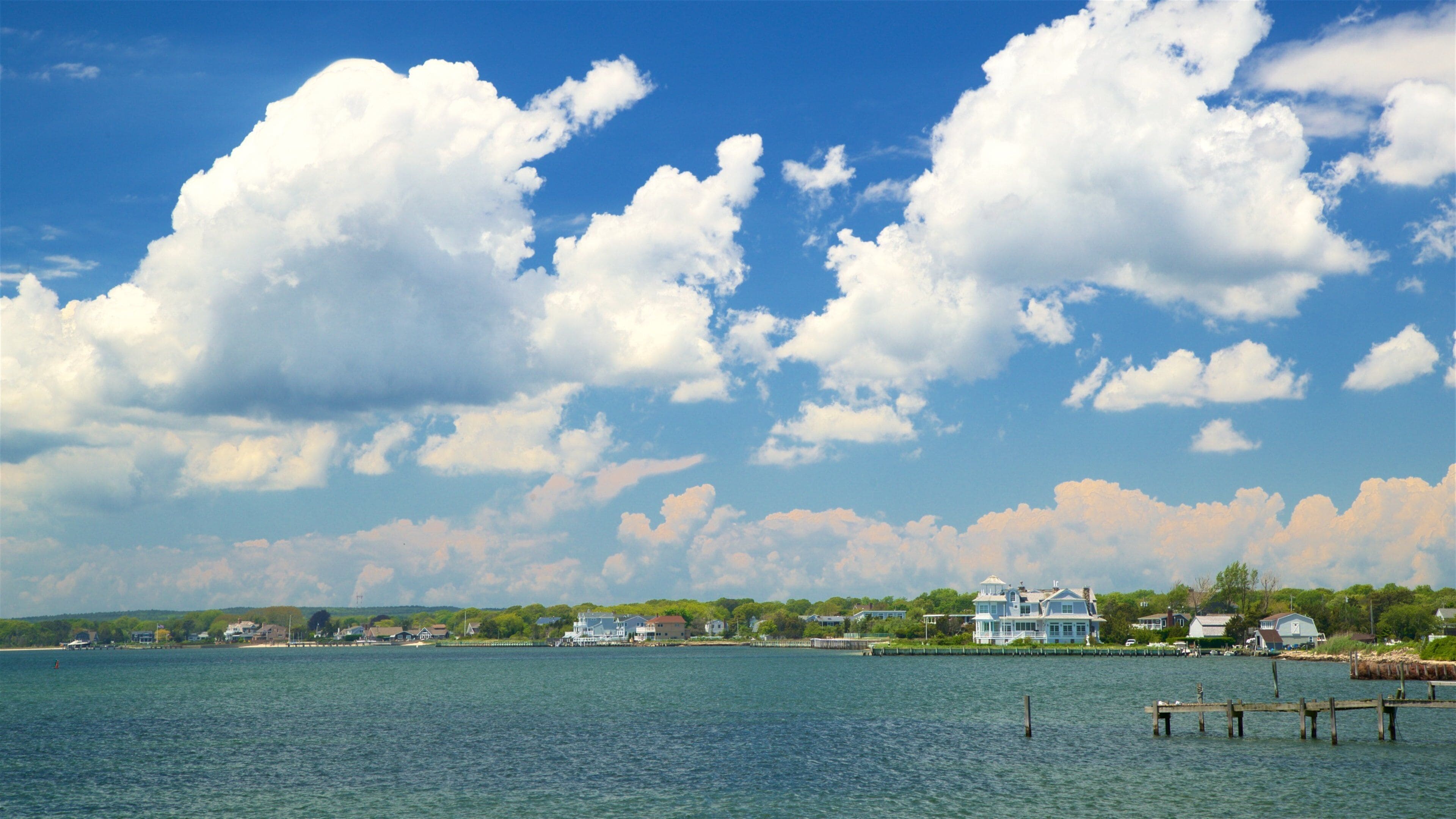 A lake with a wooden dock, a large white house, and a town with houses and greenery in the background.