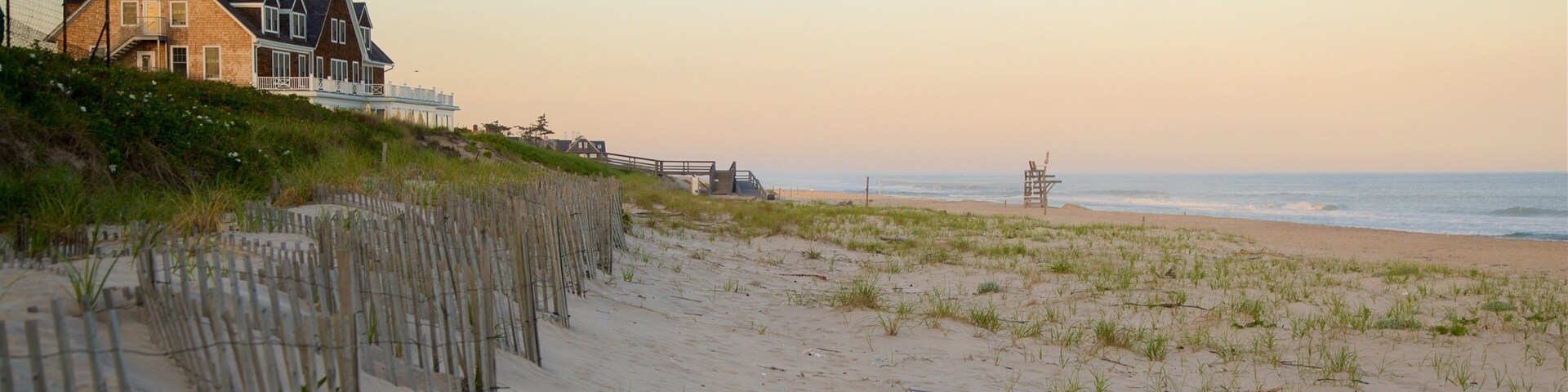 A beach with a wooden fence, a lifeguard tower, and a house with a balcony overlooking the ocean.