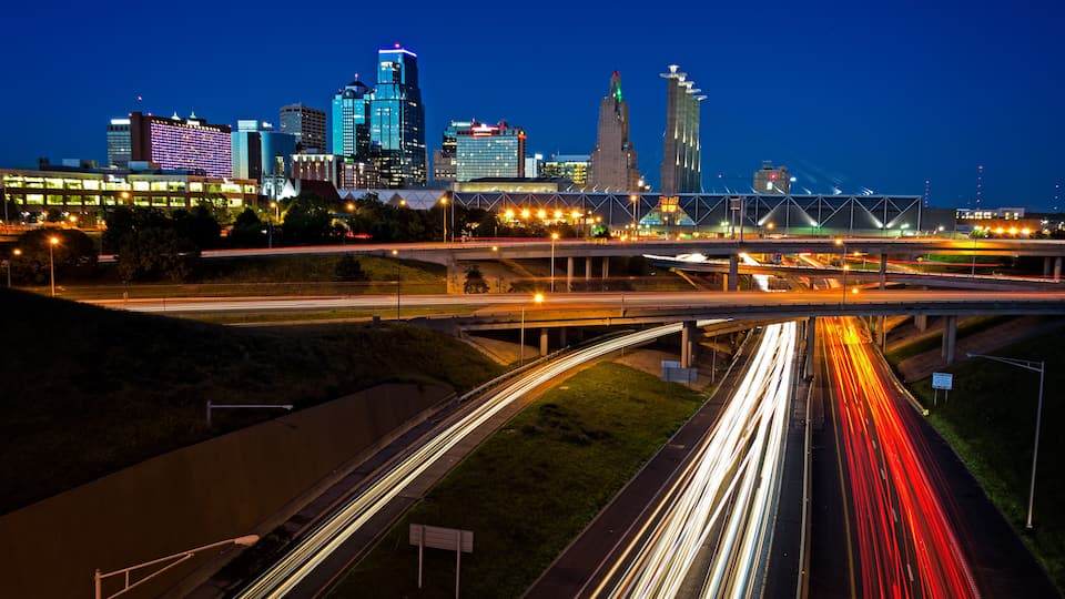 A city skyline with illuminated buildings and a multi-level highway with light trails.