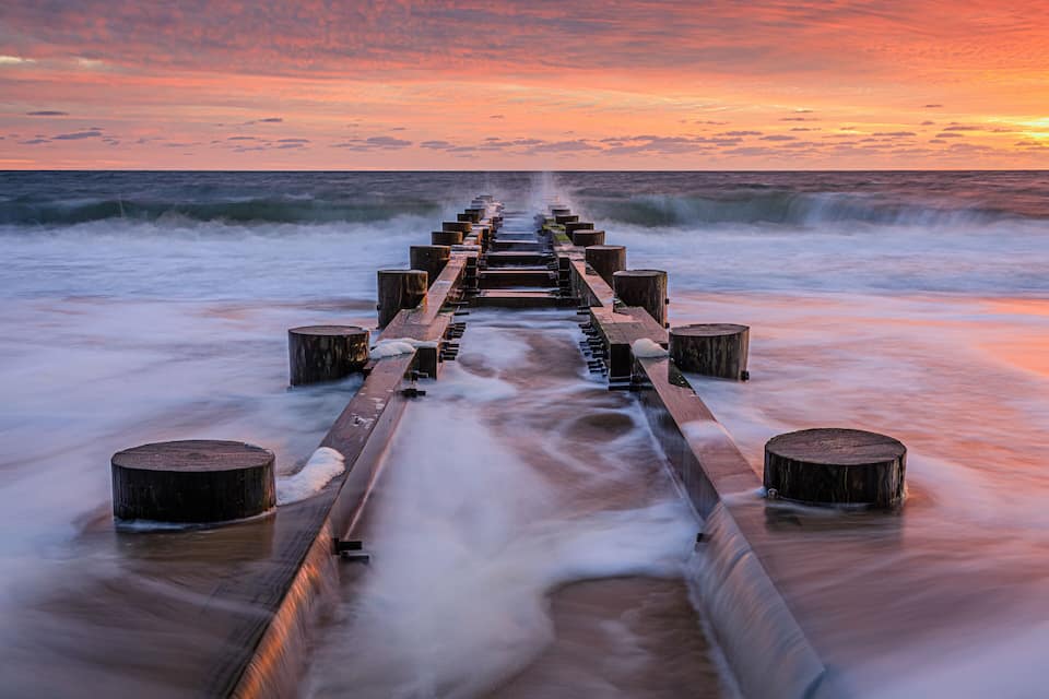 A wooden pier extending into the ocean at sunset.