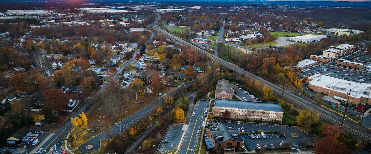 An aerial view of a town with a highway, buildings, and autumn-colored trees.