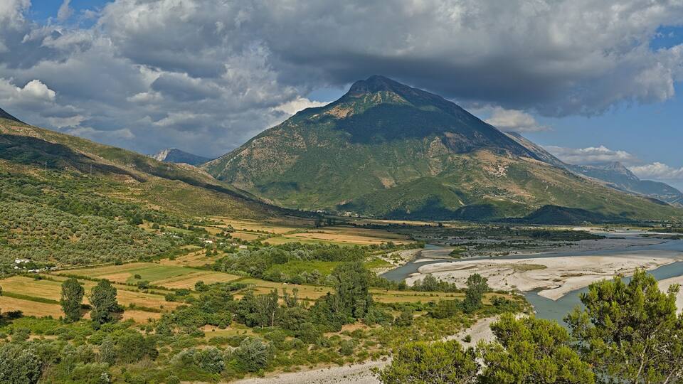A mountainous landscape with a river, fields, and scattered houses.