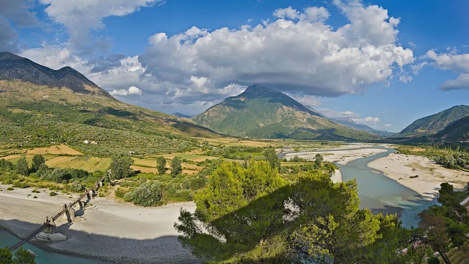 A river flowing through a mountainous landscape with a bridge and a winding road.
