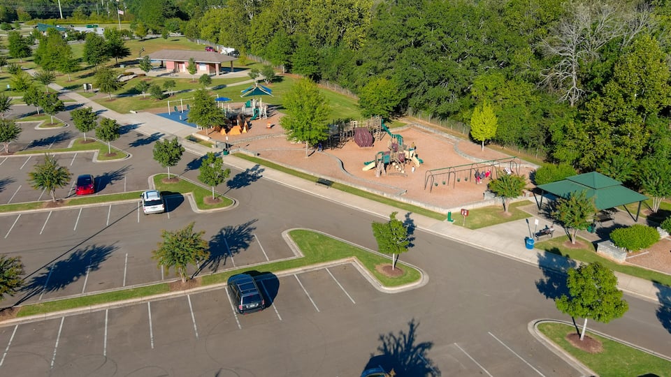 A parking lot with trees, a playground, and a building with a green roof.