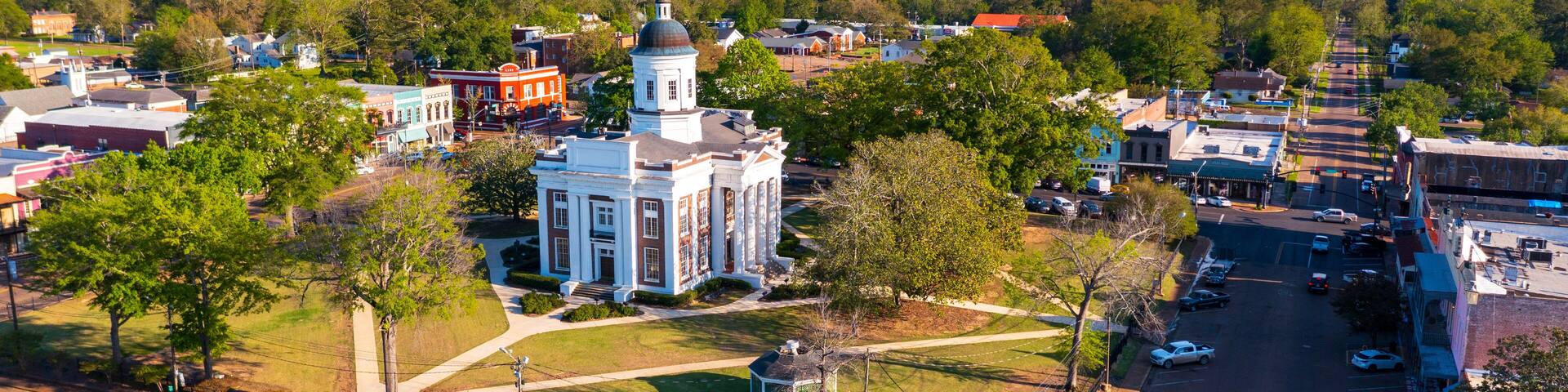 A town with a prominent white church with a dome, surrounded by green spaces and a parking lot.