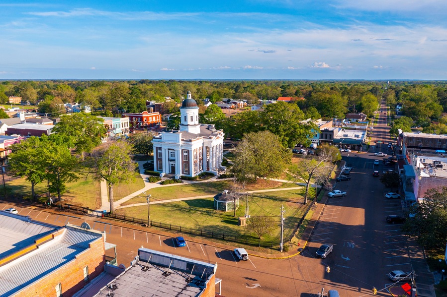 A town with a prominent white church with a dome, surrounded by green spaces and a parking lot.