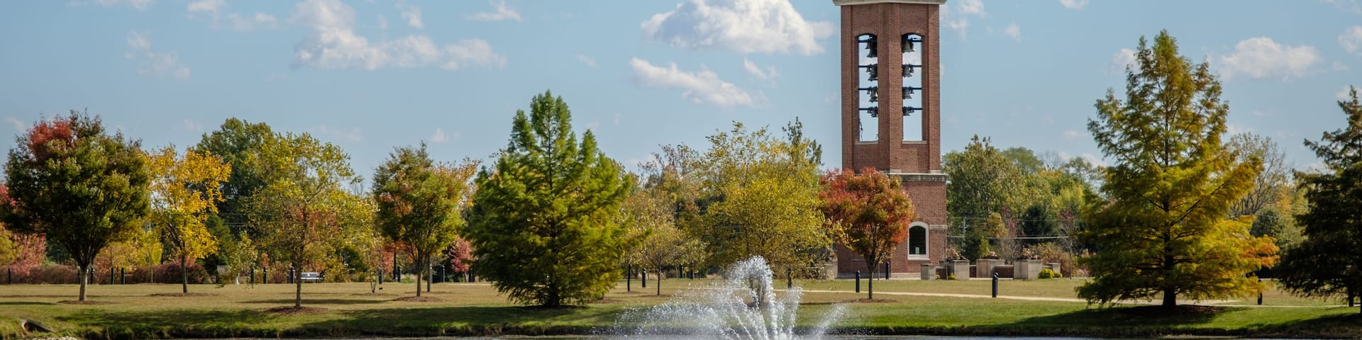 A tower with a clock, a fountain, and trees with autumn leaves.