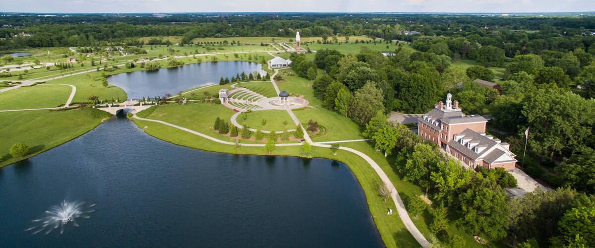 A large lake surrounded by manicured lawns, a gazebo, and a historic building with a tower.
