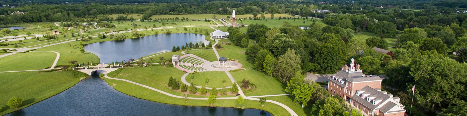 A large lake surrounded by manicured lawns, a gazebo, and a historic building with a tower.