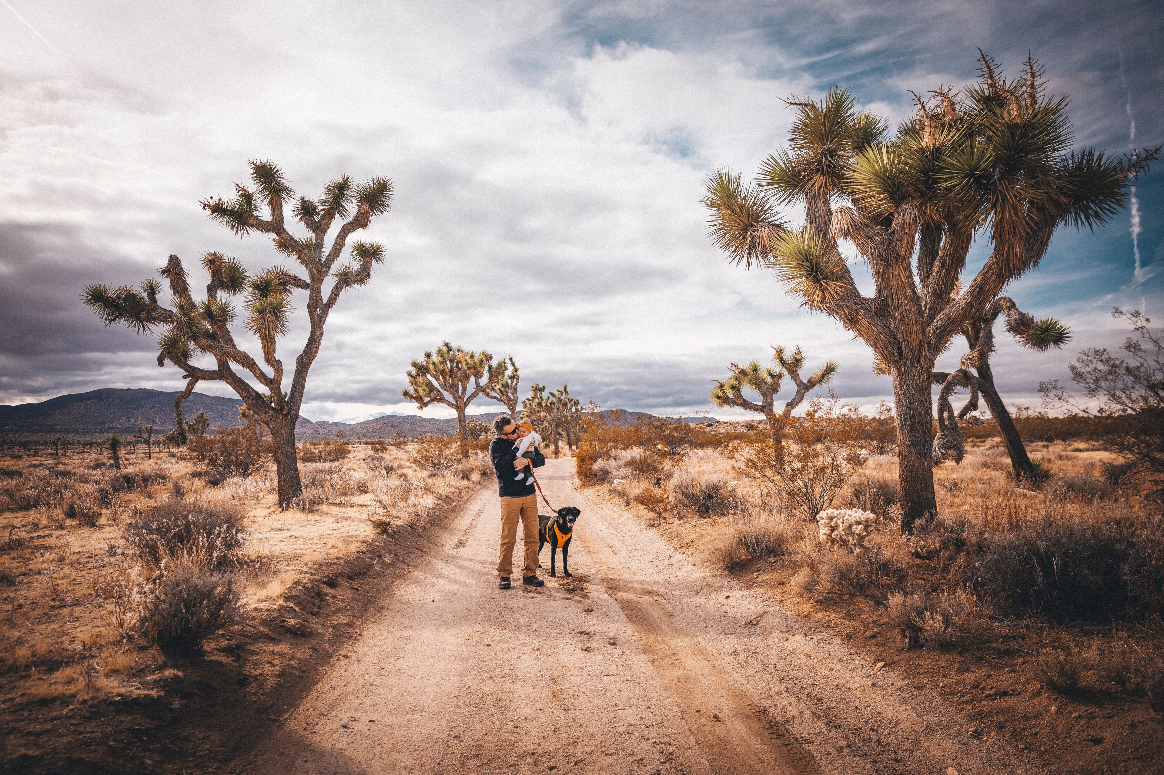 A man with a baby and a dog is standing in a desert of California