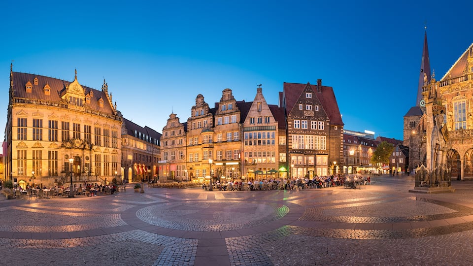 A historic European square with cobblestone pavement, ornate buildings, and a prominent church steeple.
