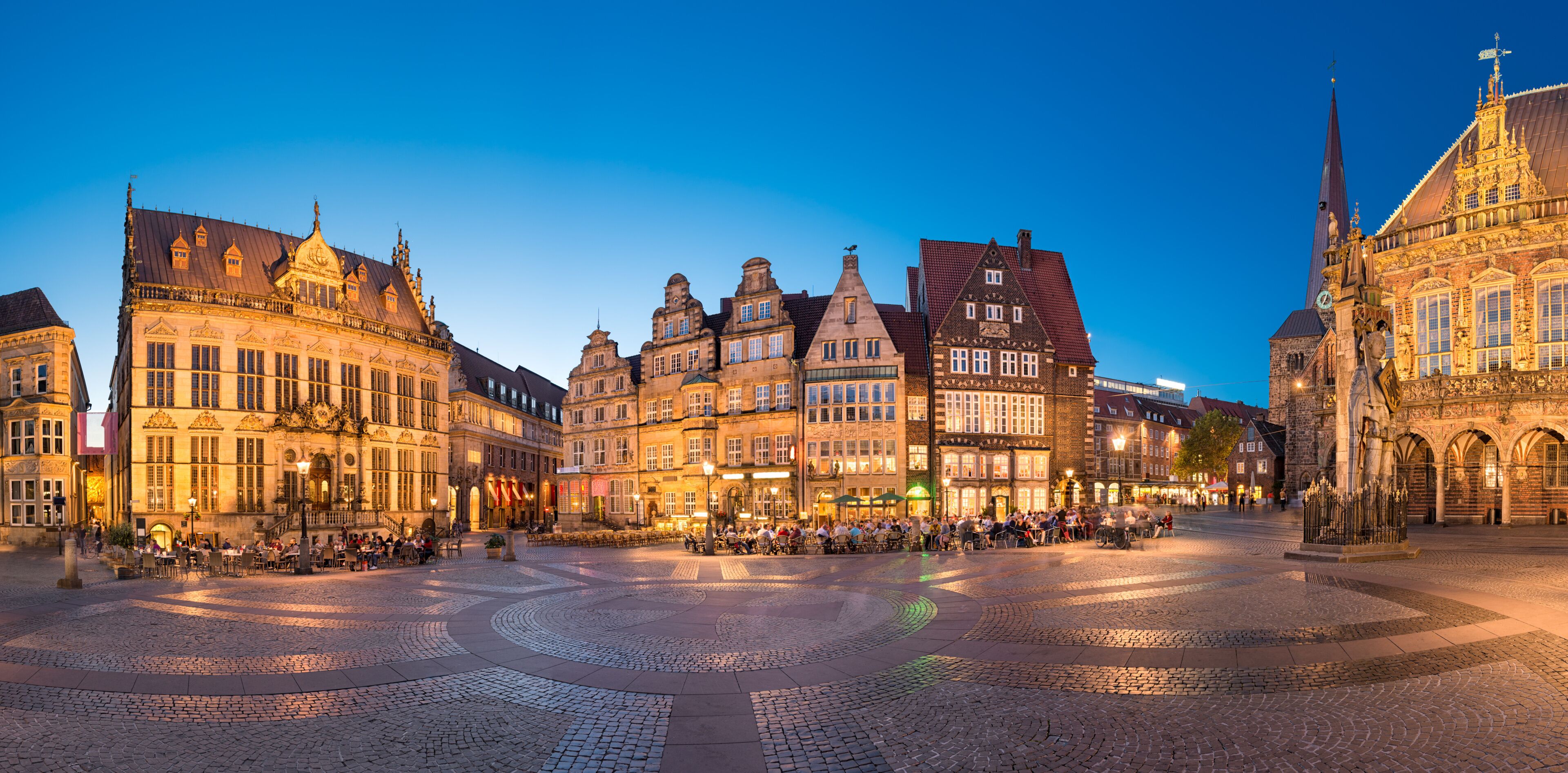 A historic European square with cobblestone pavement, ornate buildings, and a prominent church steeple.