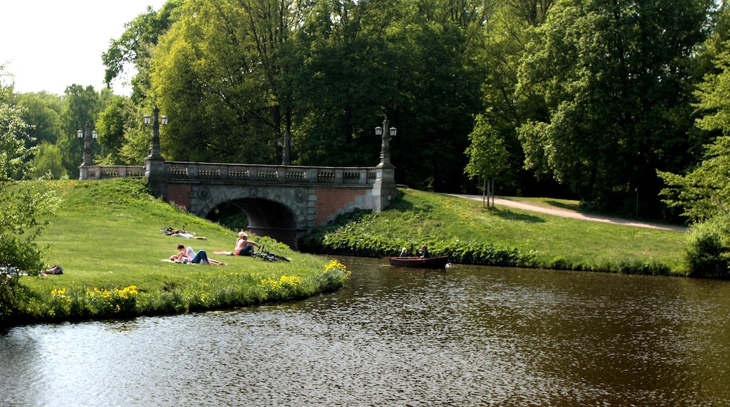 Un parc avec un pont de pierre, une rivière paisible et des gens qui se détendent sur l’herbe.