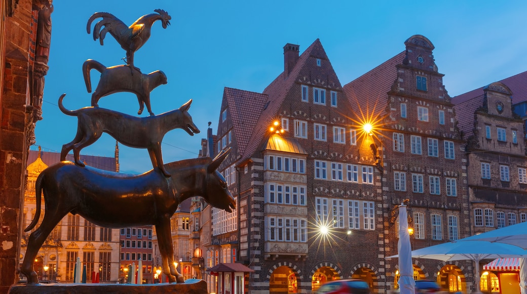 Una plaza histórica de un pueblo europeo, con una estatua destacada de un caballo y un carnero, edificios tradicionales con entramado de madera y un cielo vespertino despejado.
