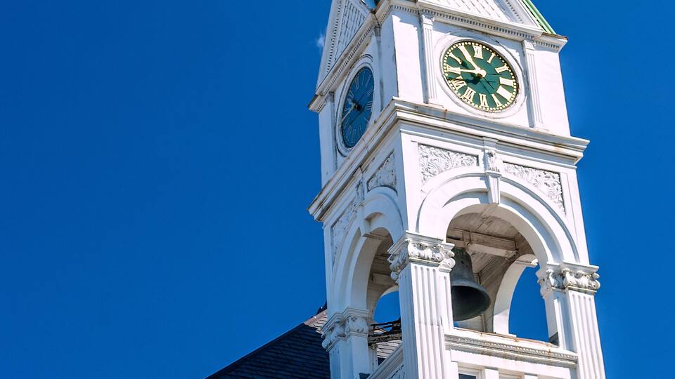 A church tower with a clock, a weather vane, and a clear blue sky.