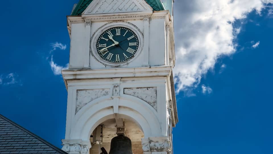 A clock tower with a green roof and a weather vane.