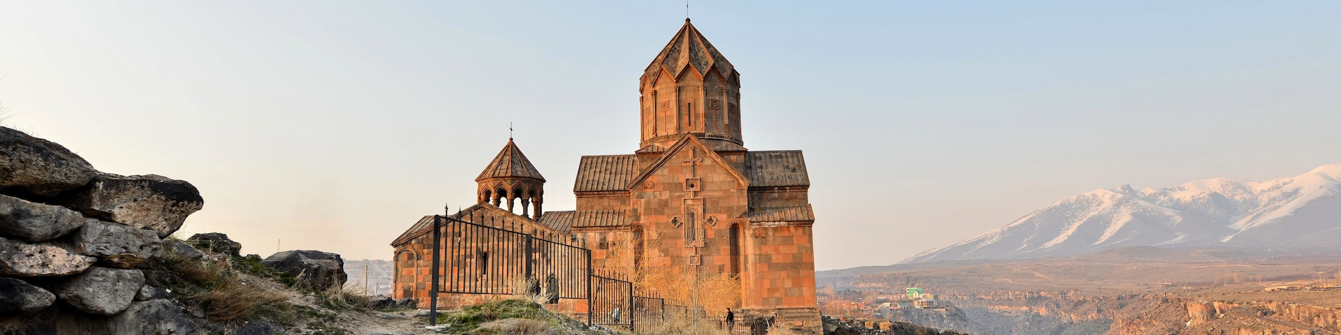 Una iglesia de piedra histórica con una imponente torre campanario, frente a un telón de montañas.