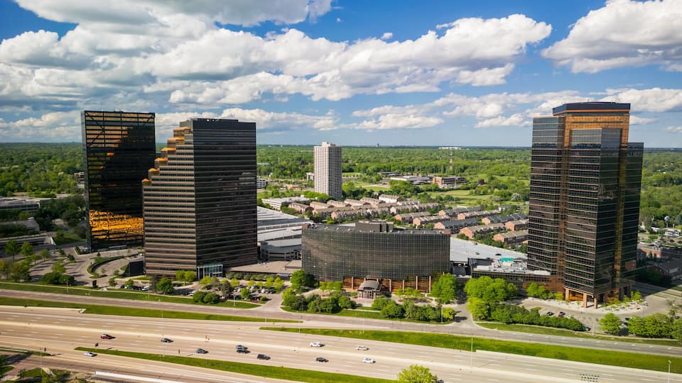 A cityscape with modern skyscrapers, a highway, and surrounding greenery.