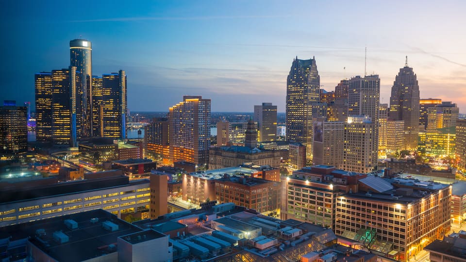 A city skyline with illuminated buildings at dusk.
