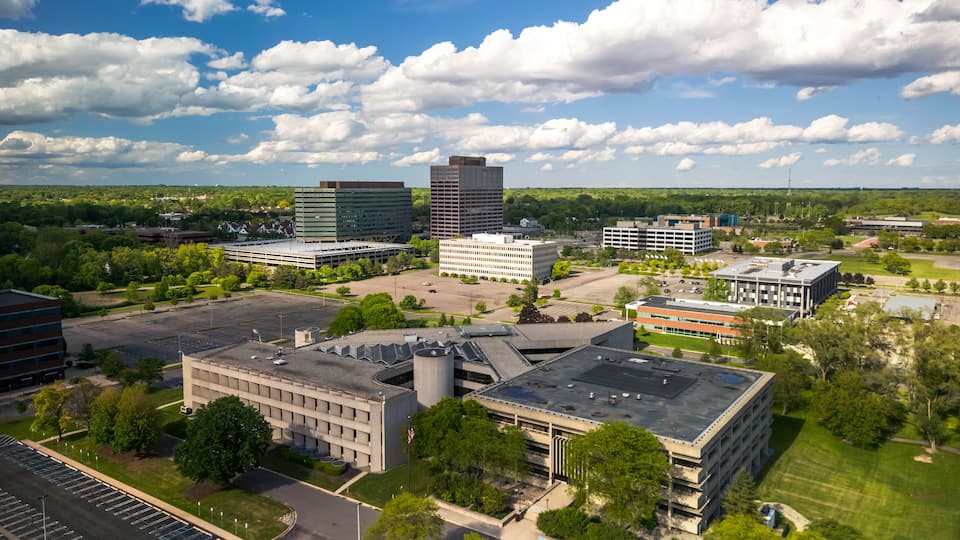 An aerial view of a cityscape with modern buildings, a parking lot, and surrounding greenery.