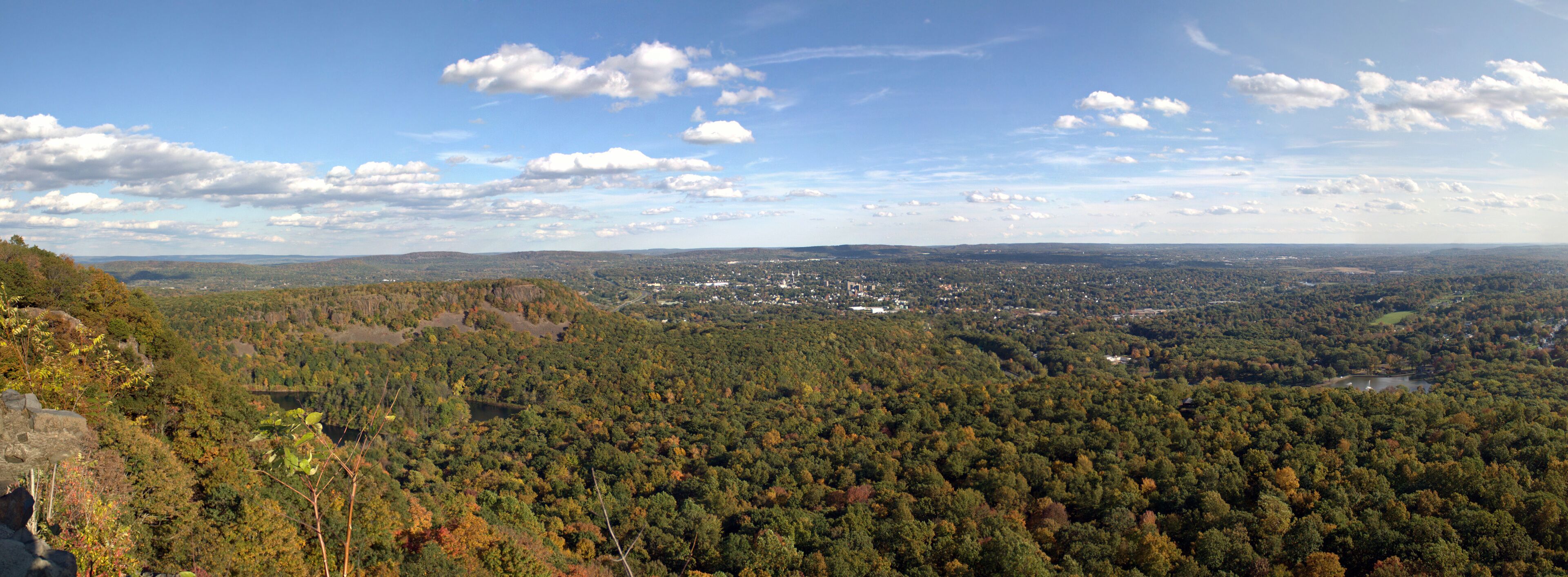 A mountainous landscape with dense forests, a small town, and a lake in the distance.