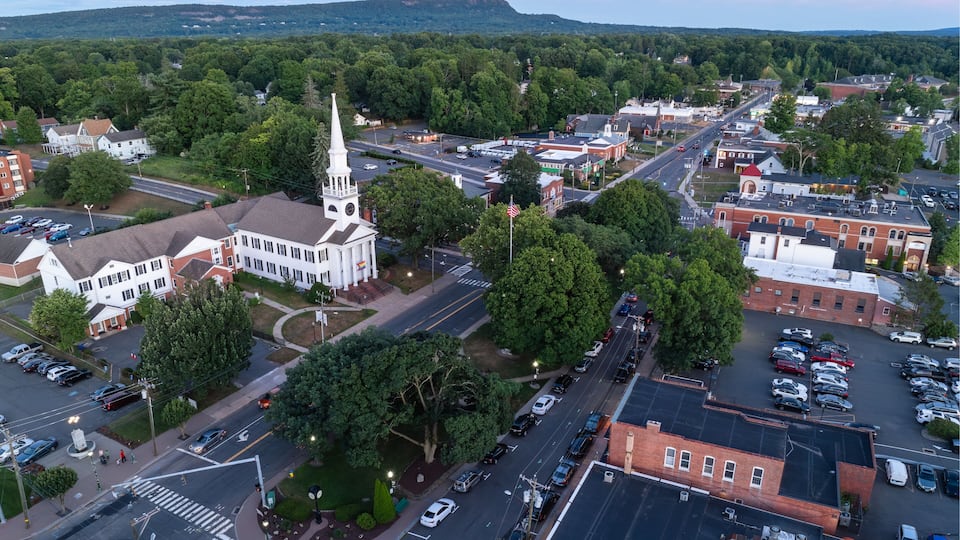 A town with a prominent church steeple, a main street, and surrounding greenery.