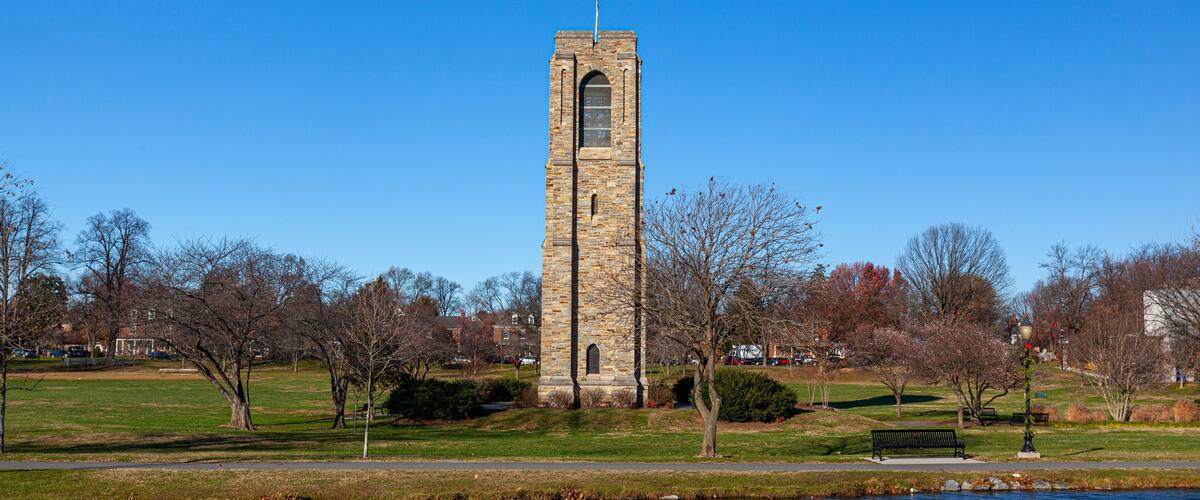 Baker Park, a city park by Carrol Creek with large open meadows, trees, walking and cycling paths and the famous historic tower and carillon. Image shows Frederick cityscape with the river.