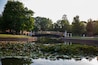 Green trees and pond with reflective surface. Pedestrian bridge over clear smooth pond. Central College campus in Pella, Iowa.